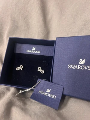 Swarovski örhängen med rosett - Supersöta örhängen från Swarovski i form av små rosetter. De är silverfärgade och glittriga med kristaller som ger extra shine. Perfekt om du vill ha något elegant och stilrent med en gullig touch. Kommer i originalask med tag.