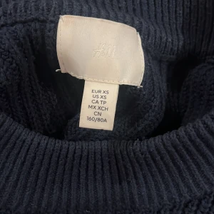Mörkblå stickad tröja från H&M - Säljer en mörkblå stickad tröja från H&M i storlek XS. Tröjan har en rund halsringning, ribbade muddar och långärmad passform. Den är loose och har en enkel, stilren design som är lätt att matcha med jeans eller andra plagg.