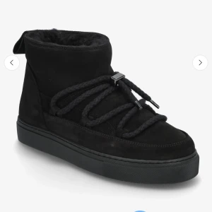 Svarta boots från Inuikii med snörning - Säljer ett par svarta boots från Inuikii med grov snörning och rund tå. Skorna har en mjuk och varm pälsfodring på insidan och är tillverkade i mocka med platt sula. Perfekta för kalla dagar och har en stilren look.