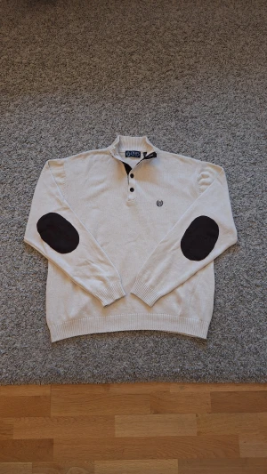Beige kofta från Chaps med knappar - Riktig snygg beige stickad tröja med halvpolokrage från CHAPS i storlek XL, men skulle nog säga den passar mer som L. 100% bomull. Använd fåtal gånger och skicket är som ny, inga defekter eller slitningar finns. Den har fyra knappar passar perfekt när du vill vara lite mer elegant. Skick: 9/10