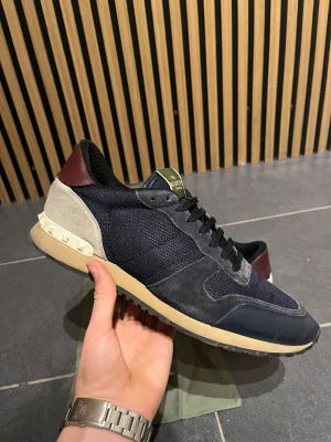 Valentino  Garavani Rockrunners - Snygga Valentino Garavani Rockrunner  i mörkblått och beige med vinröda detaljer på hälen. Ovandelen är i mesh och mocka, med skinnpaneler och klassisk snörning. . Perfekt för dig som gillar exklusiva sneakers med unik design. Kommer även med dustbag, om ni funderar över något så är det bara att fråga. 