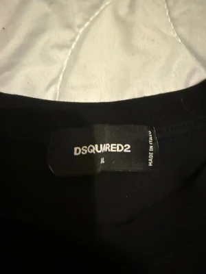 Svart DSQUARED2 ICON t-shirt XL - Svart t-shirt från DSQUARED2 i storlek XL med vit 'ICON' print på bröstet. Klassisk rund hals och korta ärmar. Tillverkad i mjuk bomull som känns skön mot huden. Snygg och stilren design som sticker ut med den feta loggan framtill.