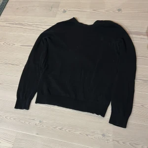 Svart stickad tröja från G-Star RAW - Svart stickad tröja från G-Star RAW med diskret logga på bröstet och metallmärke vid nacken. Tröjan har rund hals, ribbade muddar och långärmad passform. Perfekt för dig som gillar stilrena och enkla plagg med snygga detaljer.