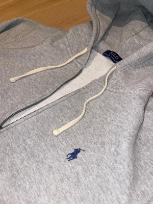 Grå Ralph Lauren Hoodie - Tja. Jag säljer min Ralph Lauren hoodie då den är för liten. Jag har i stort sätt knappt använt denna, då den mesta dels bara varit på min hylla i garderoben. Nypris på tröjan är 2200kr, skulle säga att den passar dig som är 170-185cm. Tröjan är typ regular fit, så rätt så casual i passformen. Ser helt ny och fräsch ut!
