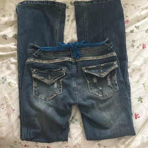 Miss me jeans - Snygga blå jeans med broderade detaljer och slitningar på bakfickorna. Byxorna har raka ben, normal passform och en blå snörning i midjan. !!!KOPIOR!!!!Dekorativa sömmar och slitna partier ger en cool look. Perfekta för dig som gillar unika detaljer.