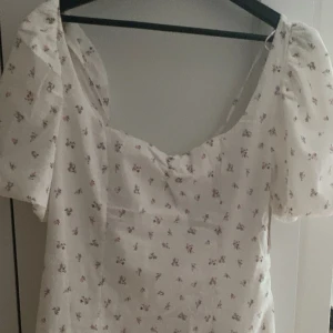 Vit blommig klänning med puffärmar - Charmig vit klänning med små rosa blommor och puffiga kortärmar. Den har en söt, romantisk stil med en lätt och luftig känsla. Perfekt för varma dagar och somriga tillfällen💗💗