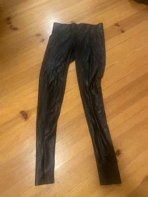 Svarta leggings i skinnimitation från Rainbow - Säljer ett par svarta leggings i skinnimitation från Rainbow. De har en tight passform och hög midja, vilket ger en snygg och edgy look. Perfekta att styla med oversized t-shirt eller hoodie för en cool vibe.