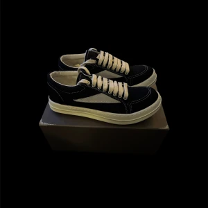 Rick Owens vans  - Snygga svarta sneakers från Rick Owens med kontrasterande vit sula och vita detaljer på sidan. Skorna har tjocka vita snören och tydliga vita sömmar som ger en cool look. Ovandelen är i textil och mocka, och sulan är platt och mönstrad för bra grepp.