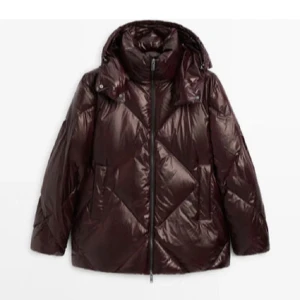 Mörkbrun pufferjacka med huva - Snygg vinröd pufferjacka från Massimo Dutti med glansig yta och stor huva. Jackan har quiltad design med stora geometriska mönster, dragkedja framtill och två sidofickor. Perfekt för kalla dagar när du vill vara både varm och stilren. Passar xs-m