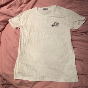 Vit t-shirt från Moncler med broderad logga - Snygg vit t-shirt från Moncler med rund hals och broderad logga på bröstet. Klassisk passform och mjukt bomullsmaterial som känns skönt mot huden. Perfekt för dig som gillar stilrena plagg med exklusiv känsla.