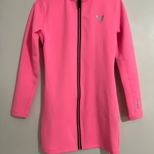 Rosa lång vindjacka från Firm Abs - Säljer en snygg och sportig lång vindjacka från Firm Abs i stark rosa färg. Jackan har hel dragkedja framtill, långärmad design och diskret logga på bröstet. Materialet är mjukt och stretchigt syntet, perfekt för träning eller chill. Fickor med dragkedja på sidorna. Det står att storlek är XL men den är så små i storlek så passa bra xs