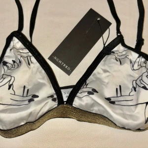  NGHTBRD bh- bralette - Snygg ball bh från NGHTBRD i vitt med svart grafiskt print av händer och svarta detaljer. Svarta kanter med en glittrig guldfärgad kant. Justerbara axelband för perfekt passform. 🚬📀                              Obs! Liten i storlek