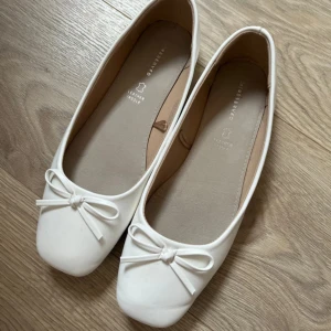 Vita ballerinaskor med rosett - Snygga vita ballerinaskor från Reserved med söt rosettdetalj framtill och rund tå. Skorna har en mjuk innersula i skinn för extra komfort och en stilren, klassisk design som passar till många outfits.