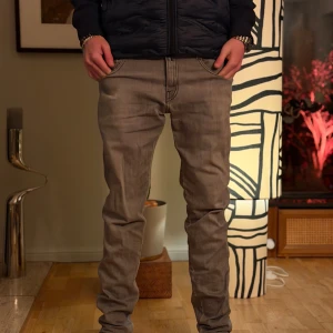 Replay grå jeans  - Snygga grå jeans från Replay med raka ben och klassisk femficksdesign. Jeansen har mörkgrå kontrastsömmar och diskret Replay-logga vid bakfickan. Perfekt för dig som gillar en stilren och avslappnad look.