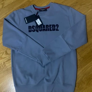 Grå sweatshirt från Dsquared2 - Snygg grå sweatshirt från Dsquared2 med svart logotyp tryckt över bröstet. Tröjan har rund hals, långa ärmar och en clean, loose passform. Perfekt för dig som gillar stilrena och trendiga märkesplagg. Materialet är mjuk bomull som känns skönt mot huden.