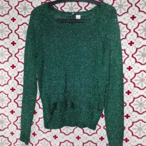 Grön glittrig stickad tröja - Snygg grön stickad tröja med glittriga inslag som ger en extra touch. Tröjan har rund hals och långa ärmar, perfekt för dig som gillar att sticka ut lite. Ribbstickad vid midja och ärmslut för en schysst passform. Passar dig som vill ha något coolt och bekvämt.