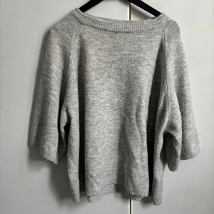 Grå stickad tröja med trekvartsärm - Mysig grå stickad tröja med trekvartsärmar och avslappnad passform. Perfekt för lager-på-lager och enkel att matcha med jeans eller kjol. Ribbstickad kant vid halsringning, ärmslut och nederkant.