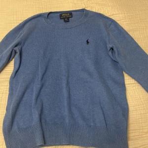 Blå tröja från Polo Ralph Lauren - Säljer en klassisk blå tröja från Polo Ralph Lauren med rund halsringning och diskret broderad logga på bröstet. Tröjan har ribbade muddar vid ärmslut och nederkant, och är perfekt för lager-på-lager-stil.
