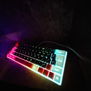 Snpurdir V600 Gaming Keyboard - Snpurdir V600 är ett kompakt gamingtangentbord med RGB-belysning och USB-C-anslutning. Tangentbordet har en snygg design med svarta, vita och orange tangenter. Levereras med USB-C kabel. Tangentbordet ser ut att vara i mycket gott skick utan synligt slitage.
