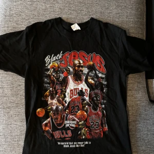 Svart Michael Jordan Bulls t-shirt - Svart t-shirt med stort tryck av Michael Jordan i olika ikoniska Bulls-poser, texten 'Black Jesus' och 'michael jordan' på framsidan. Flera basketmotiv och detaljer i rött, vitt och gult. Klassisk passform och rund hals. Perfekt för basketfans!