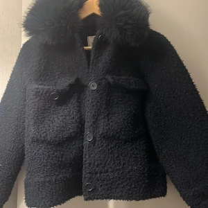 Marinblå teddyjacka från Gina Tricot - Marinblå teddyjacka från Gina Tricot med fluffig krage och stora framfickor. Jackan har knappar framtill och är tillverkad i ett mjukt, teddy-liknande material som ger en mysig vibe. Jackan är i storlek 154/162 men passar mig som är en S/M. Köparen står för frakten (69kr)! 
