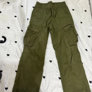 Olivgröna cargopants med fickor - Säljer ett par olivgröna cargopants med flera stora fickor på sidorna och elastisk midja. Byxorna har en avslappnad passform och är perfekta för en chill och street-inspirerad stil. Materialet är mjukt och slitstarkt, vilket gör dem sköna att bära hela dagen.