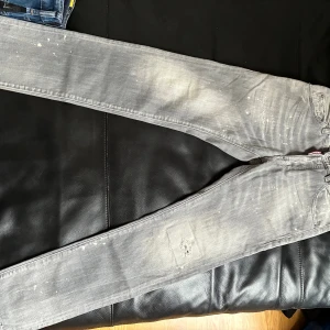 Grå Dsquared2 jeans med slitningar - Säljer ett par grå jeans från Dsquared2 med coola slitningar och blekta detaljer. Byxorna har smal passform och klassisk femficksdesign. 