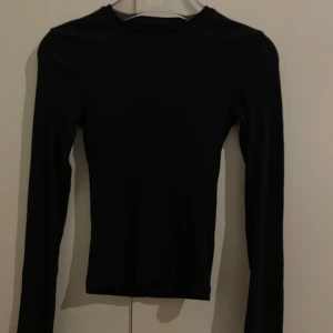 Svart långärmad topp från Bikbok - Svart långärmad ribbad topp från Bikbok i storlek XS. Enkel och stilren design med rund hals och tight passform. Materialet är mjukt och stretchigt, perfekt att matcha med jeans eller kjol. Snygg basic som funkar till många olika looks.