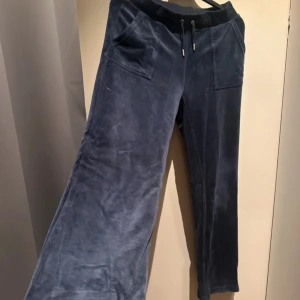Mörkblå mjukisbyxor Juicy Couture - Snygga mörkblå mjukisbyxor från Juicy Couture i mjuk sammet med broderad logga på fickan. Byxorna har snörning i midjan, stora framfickor och bakfickor med knappar.  Använda ett par gånger men inga skador 