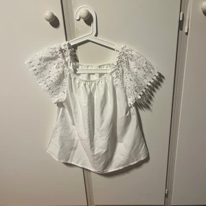 Vit blus med spetsärmar, storlek M - Säljer en vit blus i storlek M med offshoulder-design och korta ärmar i vacker spets. Blusen har elastisk halsringning och spetsdetaljer vid axelbanden. Perfekt för dig som gillar romantisk och feminin stil. Materialet känns lätt och luftigt.