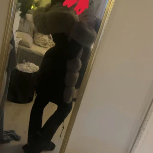 Svart jacka med grå pälsdetaljer - Säljer en svart jacka med stora, fluffiga grå pälsdetaljer längs kragen och ärmarna. Jackan har en snygg och modern look med dragsko i midjan för extra passform. Perfekt för dig som vill sticka ut och hålla dig varm under kalla dagar.