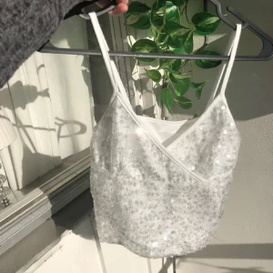 Vit paljettbeströdd croppad linnetopp - Supersöt vit linne-topp med smala axelband och v-ringning. toppen är täckt av paljetter som är genomskinliga/ ingen färg på dom så ser mer ut som ”glitter” (som på bilden). Den är S men passar säkert M oxå.