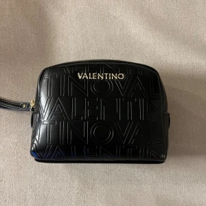Svart Valentino sminkväska - Snygg Valentino sminkväska med präglad logotyp över hela väskan och guldfärgad dragkedja. Helt ny, provad en gång. 