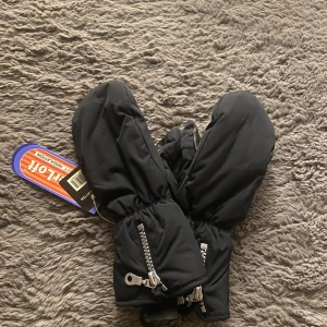 Svarta tumvantar från SmartCaz - Svarta tumvantar från SmartCaz med HyperLoft isolering, dragkedja vid handleden och mjukt pälsfoder på insidan. Utsidan är i slitstark syntet och handflatan i skinn för extra grepp. Perfekta för kalla vinterdagar när du vill hålla händerna varma.