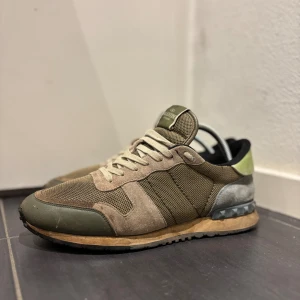 Valentino Rockrunner sneakers i beige - Äkhetsbevis finns möjligt!!Säljer ett par Valentino Rockrunner sneakers i beige, olivgrönt och grått med detaljer i mocka, mesh och skinn. Skorna har snörning, platt sula och coola nitar på hälen. Perfekta för dig som gillar exklusiva märken. Pris kan diskuteras vid snabb affär! Tveka inte att höra av dig vid eventuell fråga!