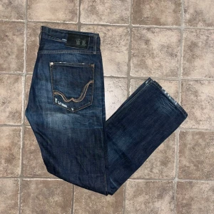 Replay jeans  - Snygga mörkblå jeans från Replay med klassisk straight fit och coola slitningar. Bakfickorna har kontrastsömmar och Replay-logga. Jeansen är tillverkade i slitstarkt bomullsjeansmaterial och har normal passform. Midja 43cm, längd 108cm. JAG SKICKAR EJ FLER BILDER NÄR JAG BÄR JEANSEN! för storleksguide hänvisar jag till måtten och för bättre inblick i passformen rekommenderar jag att googla på modellnamnet. Jeansen kan vara uppsydda utan att jag noterat det så kolla måtten noggrant :) s4