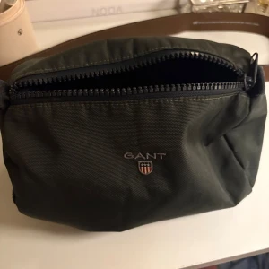 Grön necessär från GANT - Mörkgrön necessär från GANT i slitstark polyester med klassisk rektangulär form. necessär  har tydlig logotyp framtill, bred dragkedja och innerfack.