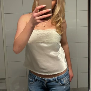 Vit satin tubtopp med spets och knyt - Supersöt vit tubtopp i satin med spetsdetaljer upptill och knytband i ryggen. Jag har sytt toppen själv och använt vid några tillfällen och fått jättemycket komplimanger. Toppen blir unik eftersom den är självgod. Priset går att diskutera och tveka inte att skriva till mig om man har några frågor💕