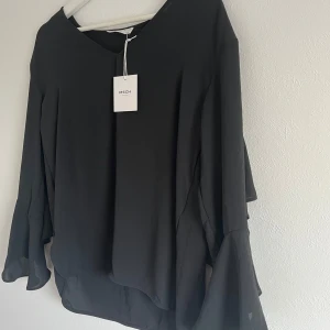 Svart blus med volang - Svart jättefin blus från MSCH copenhagen med v-ringning. Den har en volang längs ärmarna och bak över ryggen. Den är aldrig använd och prislappen sitter kvar 💕