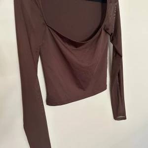 Brun mesh topp från Nelly - Säljer en brun långärmad mesh topp från Nelly. Toppen har en djup, rundad urringning och är croppad i modellen. Tunt och lätt material som ger en trendig look, perfekt att styla med höga jeans eller kjol.