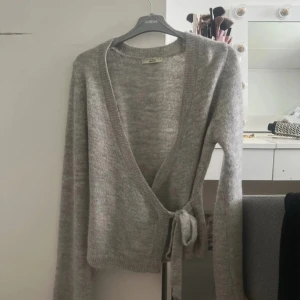Grå omlottkofta från Gina Tricot - Mysig grå omlottkofta från Gina Tricot med knyt i sidan och lång ärm. Max använd 3 gånger, den är som ny.