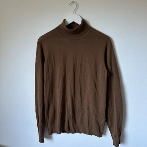 Brun polotröja i ull från Uniqlo - Snygg brun polotröja från Uniqlo i 100% ull. Tröjan har lång ärm och klassisk polokrage, perfekt för lager-på-lager. Enkel och stilren design som funkar till många outfits. 3S13