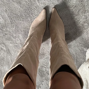 Beige knähöga boots med spetsig tå - Snygga knähöga boots i beige mocka-look med spetsig tå och blockklack. Säljer då jag aldrig fått användning av dom. 8cm klack men bekväma att gå i. Nypris 800-900kr.