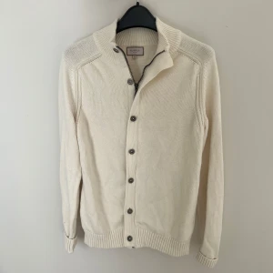 Vit full zip från Murrey i bomull - Säljer en stilren vit kofta från Murrey i 100% bomull. Koftan har ribbade muddar, dragkedja och knappar framtill samt hög krage. Perfekt för lager-på-lager och passar till många olika outfits. Det är storlek M men passar även S