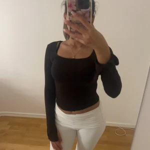 Brun långärmad croppad topp - Säljer en brun långärmad croppad topp med fyrkantig halsringning. Toppen har en slim passform och är tillverkad i ett mjukt, stretchigt material som sitter snyggt mot kroppen. Ärmarna har en liten slits vid handleden för extra detalj.