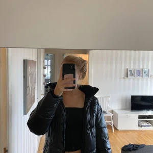 Svart pufferjacka från Lindex - Säljer en svart pufferjacka från Lindex i storlek 170. Jackan har huva, dragkedja och är quiltad för extra värme. Materialet är glansigt och vattenavvisande, perfekt för kalla dagar. Enkel och stilren design som passar till det mesta.