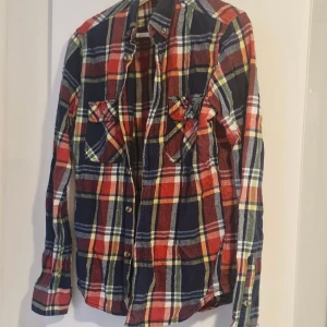 Rutig skjorta från Bondelid, S - Snygg rutig skjorta från Bondelid i storlek S. Skjortan har klassiskt mönster i marinblått, rött, grönt och vitt, med två bröstfickor och knappar framtill. Tillverkad i mjuk bomull, perfekt för en chill och avslappnad stil.
