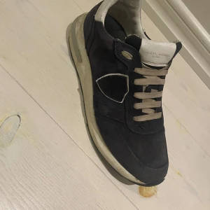 Philippe Model svarta sneakers mocka - Snygga svarta sneakers från Philippe Model med beige detaljer och snörning. Ovandelen är i mjuk mocka och har en rund tå. Skorna har en vit och svart sula med mönstrad undersida för extra grepp. Perfekt för dig som gillar stilrena och exklusiva sneakers.