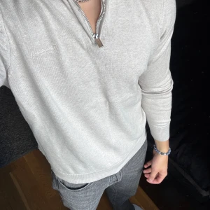 Beige halfzip tröja från Bondelid - Säljer en Beige stickad tröja från Bondelid med halv dragkedja och broderad logga på bröstet. Tröjan har lång ärm, ribbade muddar och klassisk krage. Perfekt för dig som gillar stilren och enkel design.