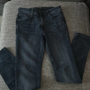 Mörkblå jeans från Jack & Jones - Snygga mörkblå jeans från Jack & Jones med klassisk femficksdesign och diskreta slitningar. Jeansen har raka ben och slim passform, tillverkade i mjukt denimtyg som sitter skönt hela dagen. Perfekta för en stilren och avslappnad look.